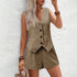Woman wearing a beige vest and shorts set against a white wall.